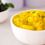 Potatoes cooked with turmeric in a white bowl with a few mint leaves on the side