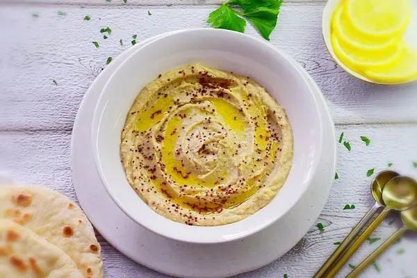 Creamy Homemade Hummus in a white bowl with pita bread and lemon on the side