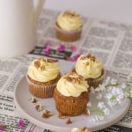 Carrot Cupcales on a white plate with pink flowers around and a vase back left