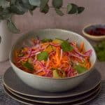 Carrot salad in a bowl with chilli at the back right and green leaves on the left