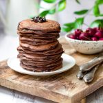 Fluffy chocolate pancakes on a white plate with cherries on the side