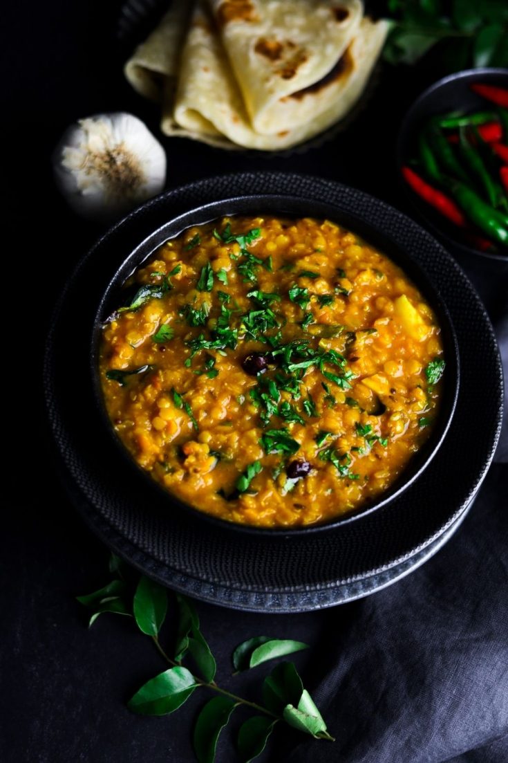 Red Lentil Dal in a black bowl with curry leaf bottom left and roti top left